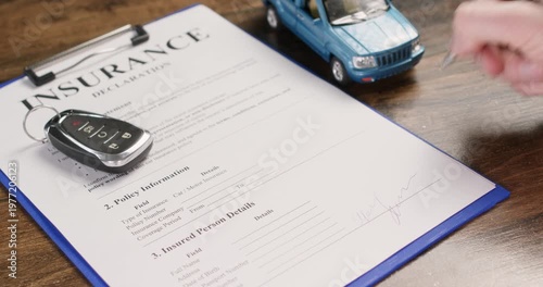 Car keys rest on insurance declaration as man signs policy form with hand. Driver puts signature completing coverage details during vehicle insurance process slow motion