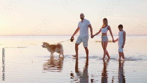Happy family walking the shore of the sea with the dog at the sunset