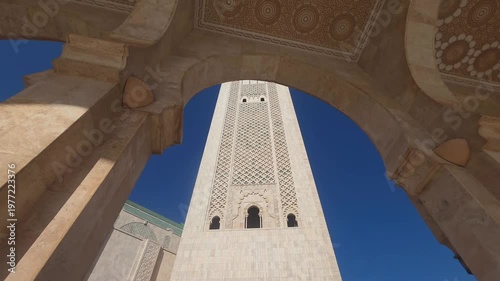 pan view of Hassan II Mosque against sky , Hassan II Mosque minaret looking up through arches - Hassan II Mosque minaret upward view through ornate arches Casablanca, Morocco