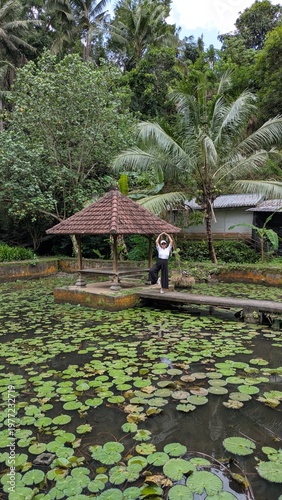 Happy female traveler in casual clothes exploring a beautiful tropical water garden and traditional bale in Bali during a sunny vacation trip