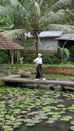 Happy female traveler in casual clothes exploring a beautiful tropical water garden and traditional bale in Bali during a sunny vacation trip