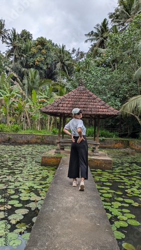 Happy female traveler in casual clothes exploring a beautiful tropical water garden and traditional bale in Bali during a sunny vacation trip
