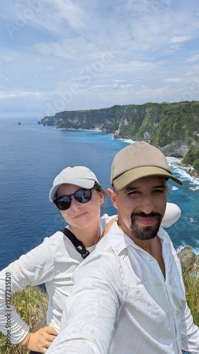 Couple taking selfie at Manta Point cliff in Bali Indonesia, tropical paradise with turquoise ocean and panoramic seascape, friends enjoying iconic viewpoint, risky edge adventure with stunning waves 