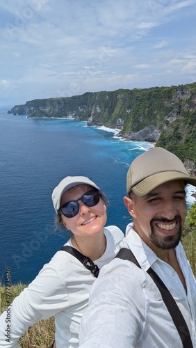 Couple taking selfie at Manta Point cliff in Bali Indonesia, tropical paradise with turquoise ocean and panoramic seascape, friends enjoying iconic viewpoint, risky edge adventure with stunning waves 