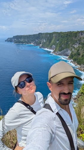 Couple taking selfie at Manta Point cliff in Bali Indonesia, tropical paradise with turquoise ocean and panoramic seascape, friends enjoying iconic viewpoint, risky edge adventure with stunning waves 