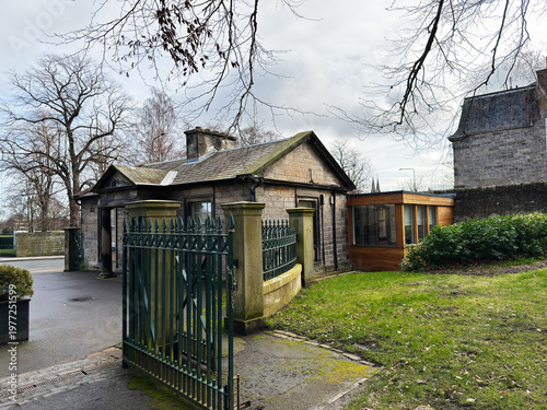 Historic gatehouse with iron gate and stone lodge beside a modern wooden extension at a garden entrance in Edinburgh, Scotland, UK