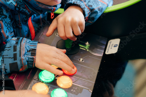 Close up of child hands playing arcade game with colorful buttons and joystick