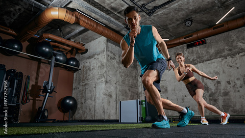 Картината върху платно Man and woman performing dynamic shuttle run exercise together in modern gym