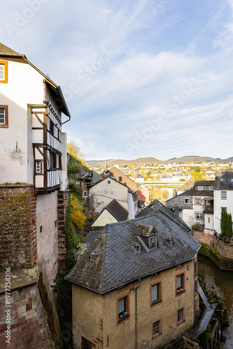 Scenic view of Saarburg with traditional houses along a narrow river, overlooking rooftops, historic architecture, and a peaceful valley landscape under a dramatic sky
