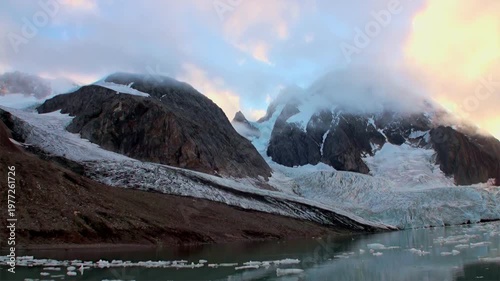 Experience Arctic landscape. Witness beauty of glacier flowing into water, surrounded by mountainous terrain in Svalbard. Serene atmosphere during polar summer makes for unforgettable expedition.