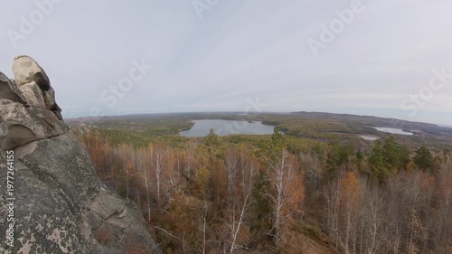 A man on a cliff. A hiker admires the picturesque autumn view of the forest and lake from a mountaintop, sitting on granite rocks.