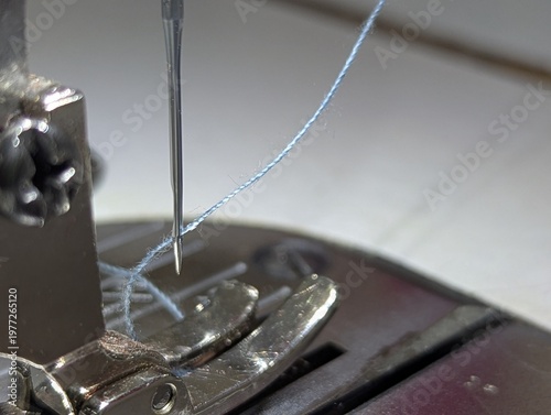 фотографія Extreme close-up of a silver sewing machine needle with blue thread, focused on the stitching process on a metal presser foot