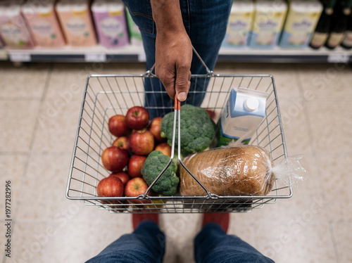 Person pushing shopping cart filled with groceries in supermarket aisle