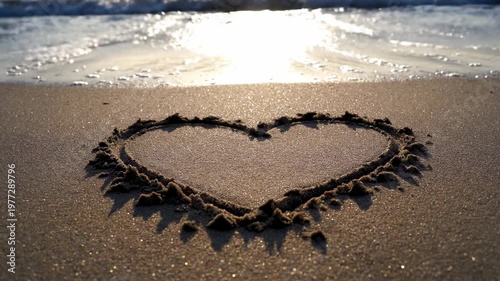 Heart drawn in sand, waves gently lap at the shore, golden light