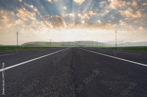 Wide-angle view of a sunset over an asphalt road. A highway winding through nature.