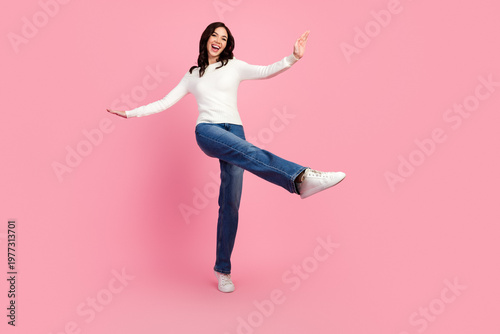 Obraz na płótnie Happy young woman in white sweater and jeans balancing playfully on one leg agai