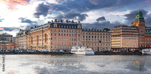 Foto Historic architecture and a passenger ferry along the scenic waterfront of Stockholm, Sweden, under a dramatic sunset sky