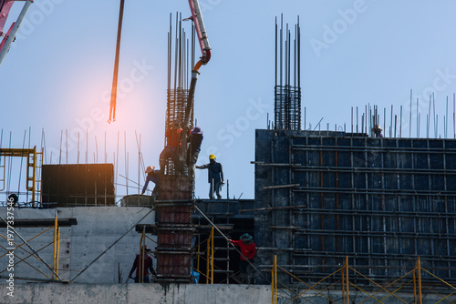 Construction workers pouring concrete into reinforced column using pump at building site with clear sky, showing teamwork and engineering process in urban development.