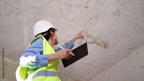 Foto Female inspector wearing safety helmet and vest examining mold growth on ceiling