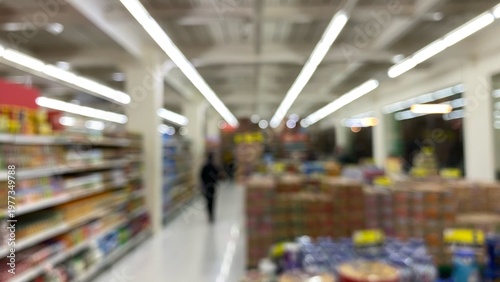A blurry supermarket interior with bright lighting and aisles of products on the left and right. A modern setting with a bokeh effect.