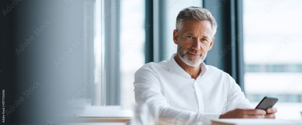 Fototapeta premium Mature businessman using smartphone indoors
