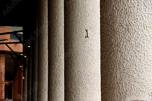 A row of grey columns supporting the projection of a building, a colonnade