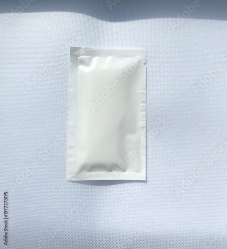 Minimal white wet wipe sachet on textured background with soft natural light, hygiene and personal care concept