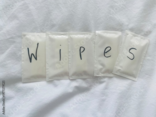 Wet wipe sachets spelling “wipes” on white background, hygiene and personal care concept