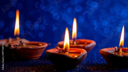 Diya oil lamp flame candle clay festival on blue background with bokeh, warm glow from four traditional clay lamps for Diwali