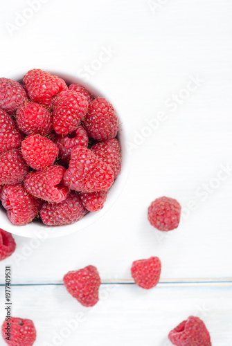 raspberry fruits at white ceramic cup, on bright wood table