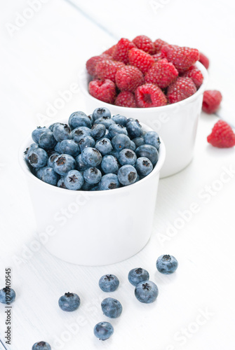 bilberry and raspberry fruits at white ceramic cup, on bright wood table