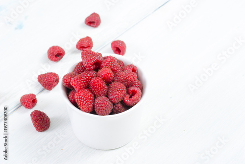 raspberry fruits at white ceramic cup, on bright wood table