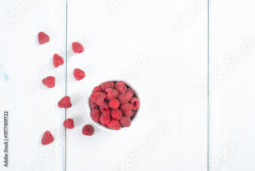 raspberry fruits at white ceramic cup, on bright wood table
