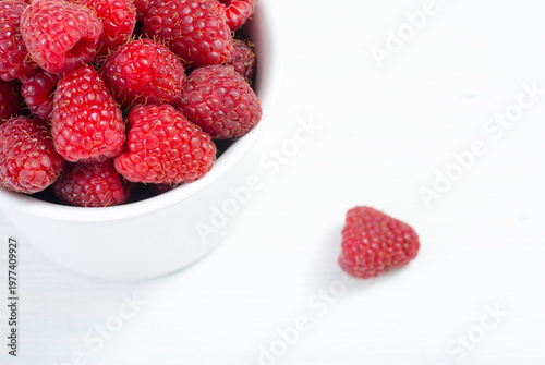 raspberry fruits at white ceramic cup, on bright wood table