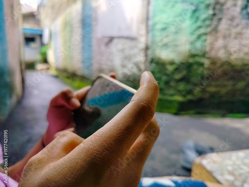 Close-up of a person holding and typing on a smartphone outdoors with a narrow alley background. Concept of mobile communication, social media browsing, and digital connection in urban environment.