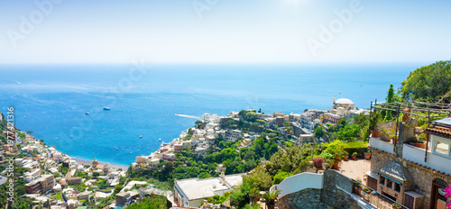 Panoramic view of Positano on Amalfi Coast, Italy with colorful buildings cascading down hillside toward turquoise Mediterranean waters. Lush vegetation frames traditional architecture of Positano 