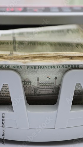 Macro shot of banknote counting machine with Indian rupee (INR) money. Automatic currency counter equipment processing 500 rupees with Red Fort vignette. Finance and banking industry in India.