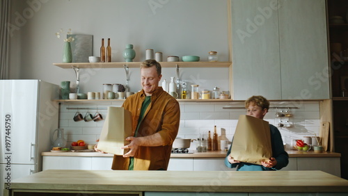Son helping father unpacking groceries on kitchen table. Helpful boy taking 