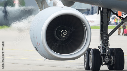 Close-up view of an aircraft engine showcasing intricate turbine details and wheel assembly at a bustling airport during daylight