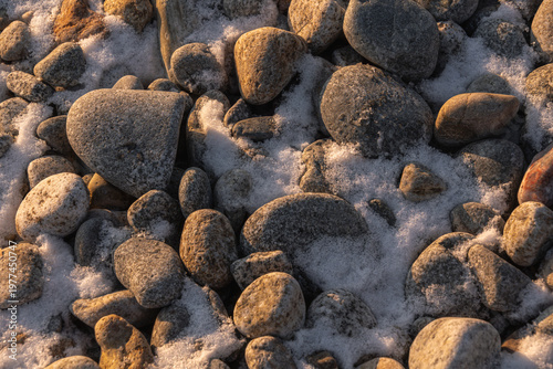 Close-up view of various smooth stones and pebbles scattered on a snowy surface, showcasing natural textures and colors in a winter landscape