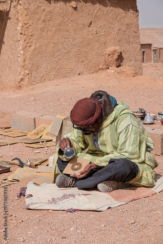 Moroccan artist burning solar drawing on paper in ait ben haddou