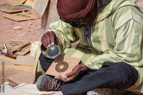 Moroccan artisan creating desert art using magnifying glass and sun