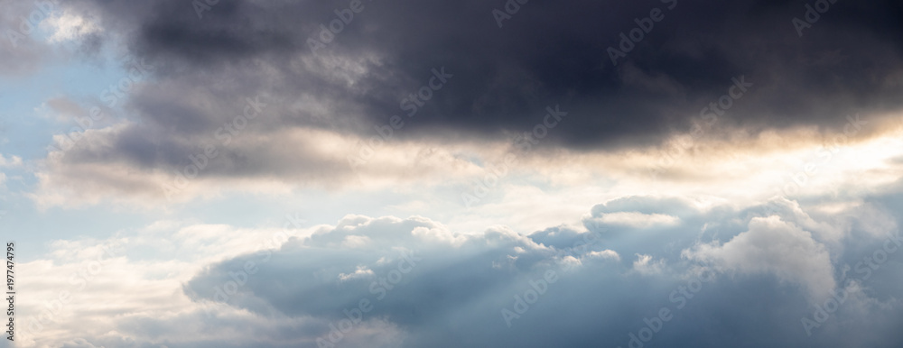 Obraz premium Panoramic stormy sky with contrast of dark and light clouds and sunbeams, dramatic atmosphere before thunderstorm
