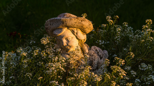 Vertäumte Aufnahme einer Steinfigur in einem Garten, welche von der Sonne angestrahlt wird.