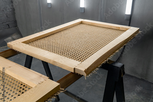 Photos Wooden frame with tightly woven rattan surface sits on a stand in a paint booth
