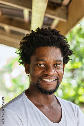 Portrait of a Smiling Young African Man with an Afro Hairstyle blurred green outdoor background.