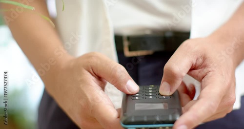Nonbinary African in shirt starting with thumbs hovering, holding keypad, tapping numbers at desk