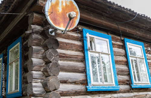 Old wooden house with blue window frames and satellite dish in rural setting