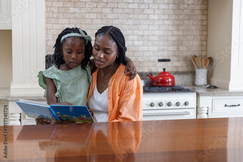 African American mother and child reading blue book at kitchen counter with red kettle