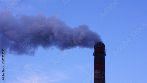 Industrial chimney emitting dark smoke into clear blue sky